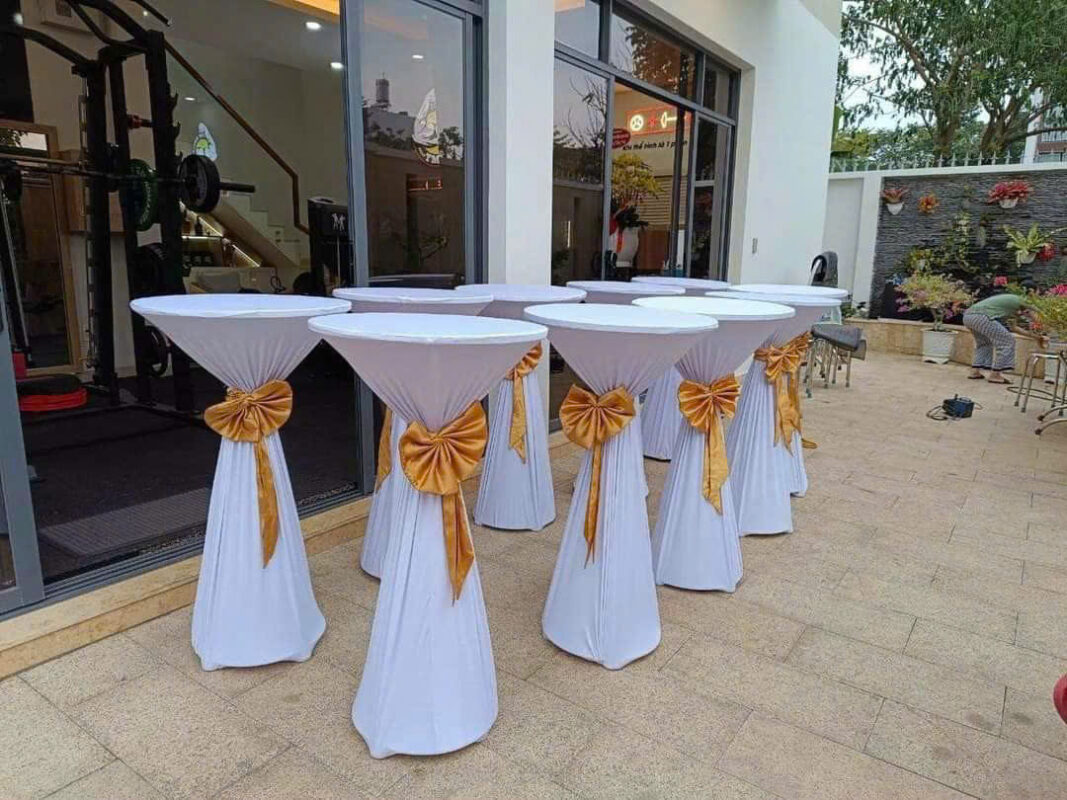 Bàn bar phủ khăn trắng và nơ vàng bố trí trước khu cửa kính